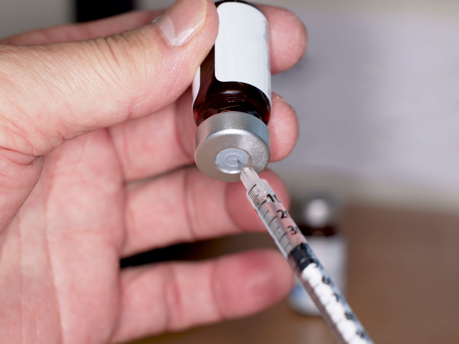 Close up of health provider's hands while drawing medication from a bottle using a syringe.