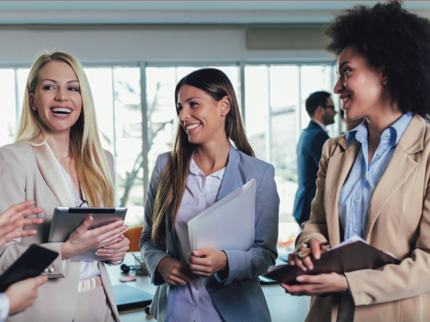 Four businesswomen talking, holding mobile computers.
