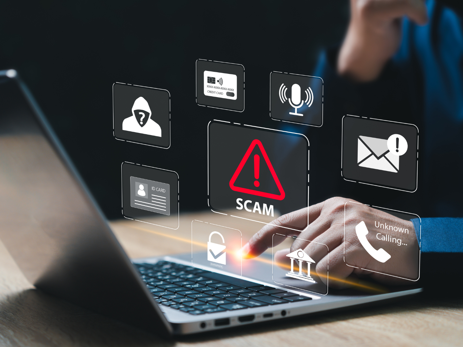 Close up view of a person's hands using a laptop computer with scam alert graphics floating above the keyboard.