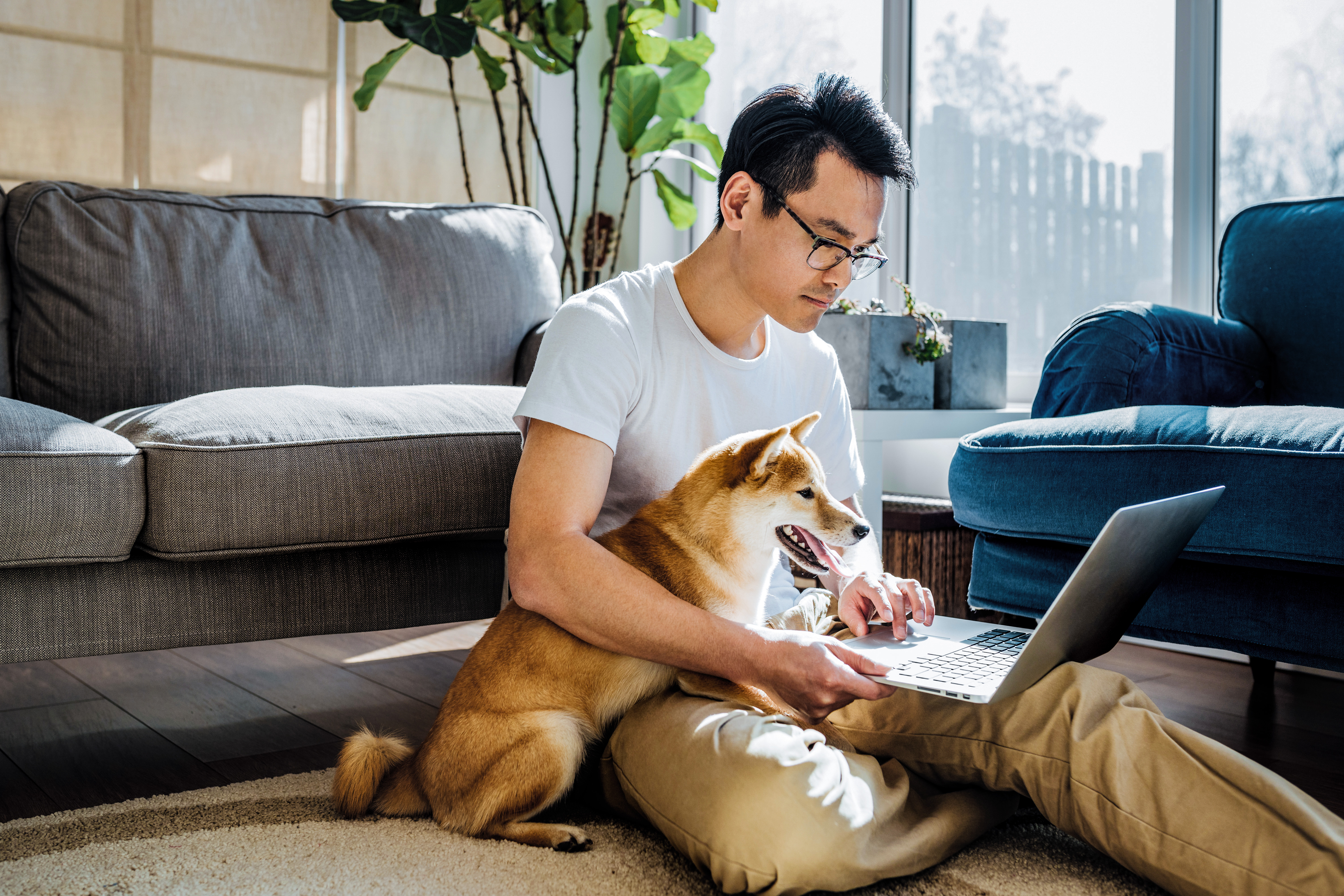 Man hugs dog as he works on a laptop on the floor