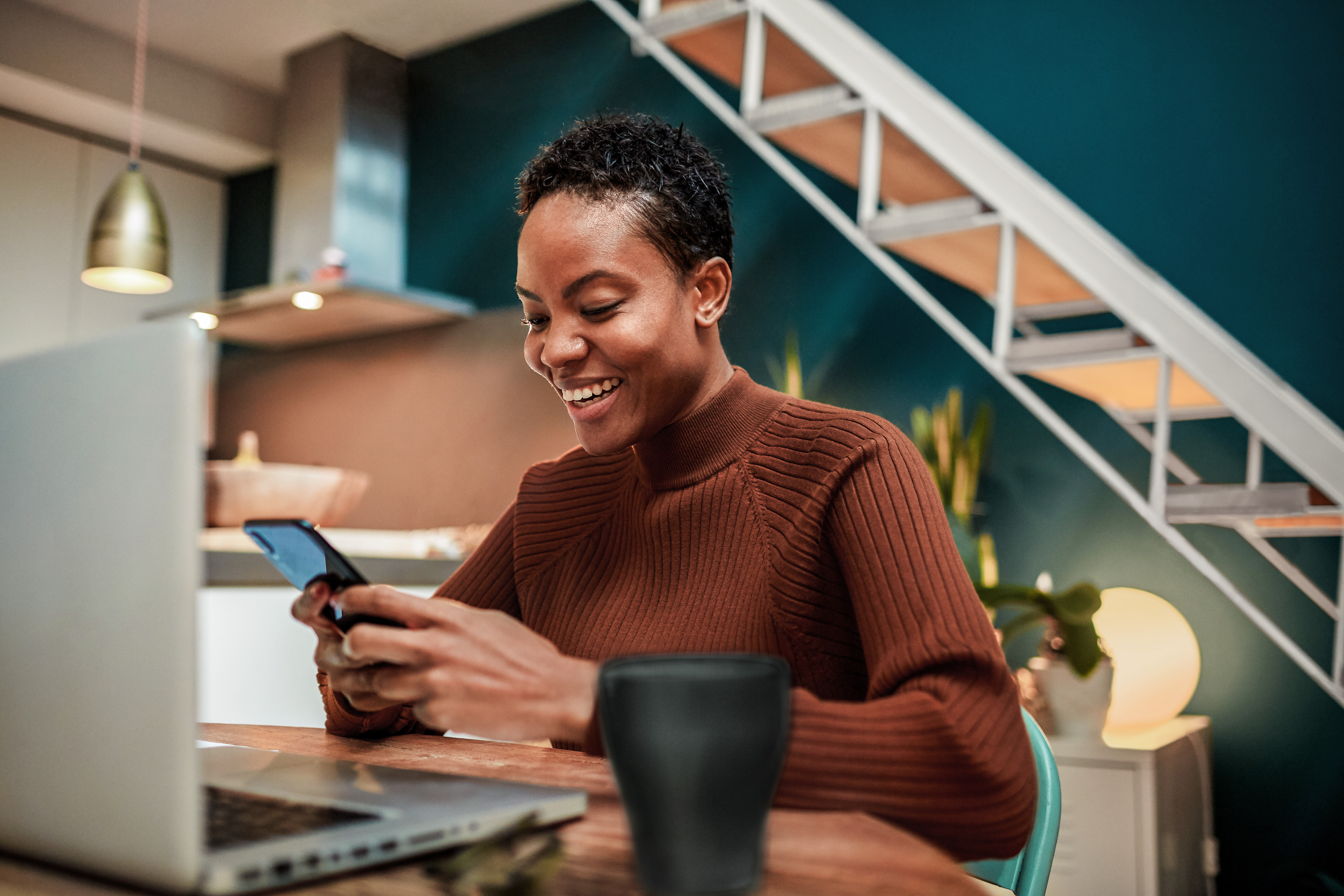 Woman laughs looking at her phone while she works on her laptop