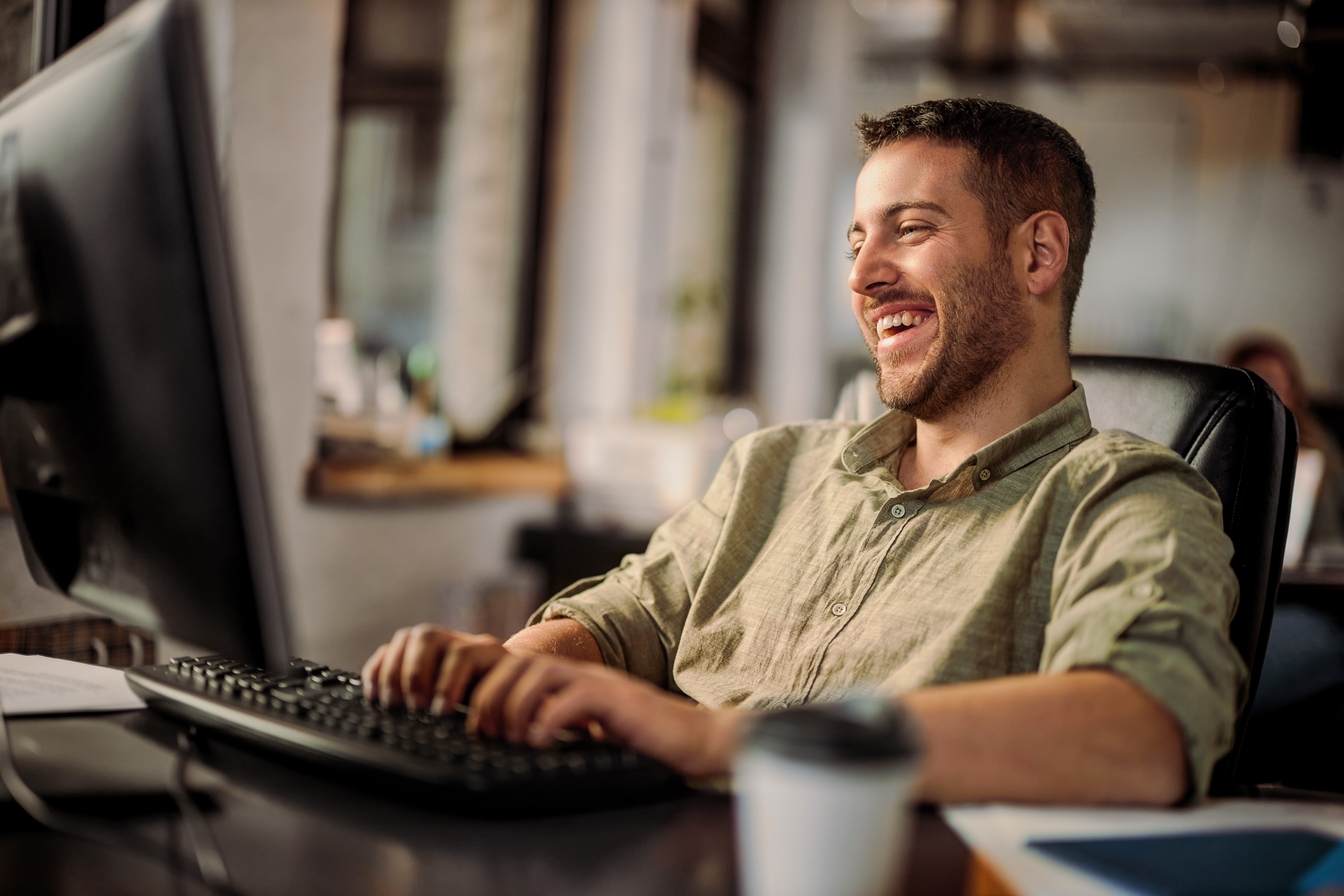 Man laughs as he types at computer desk